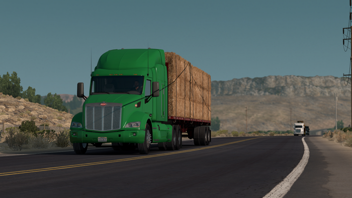 Green Peterbilt truck hauling hay bales on a highway