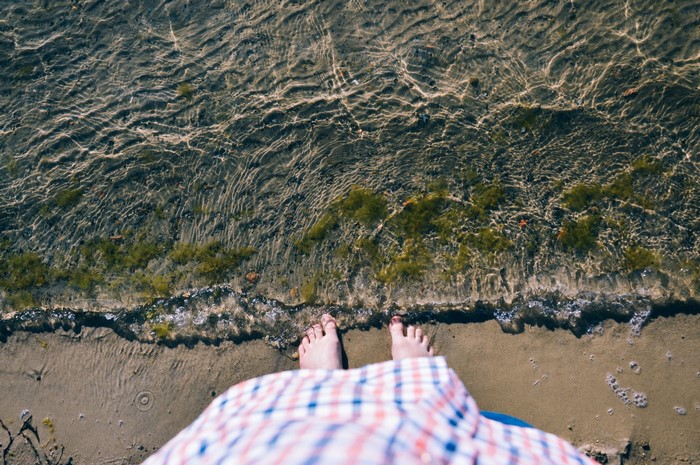 Feet standing at the edge of the water on a sandy shore