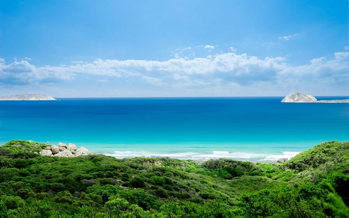 Green hills meet the turquoise ocean under a blue sky with clouds