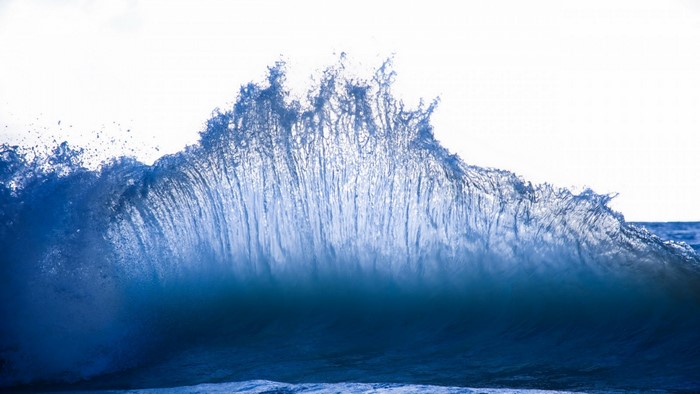 A large blue wave crashing with sunlight shining through