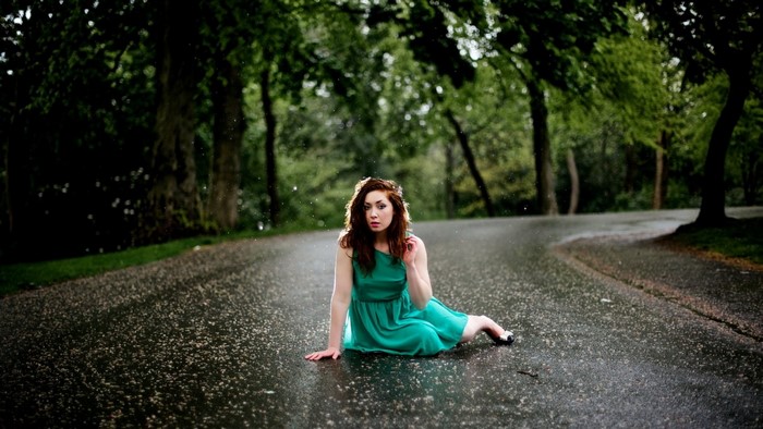 Woman in green dress sitting on wet road