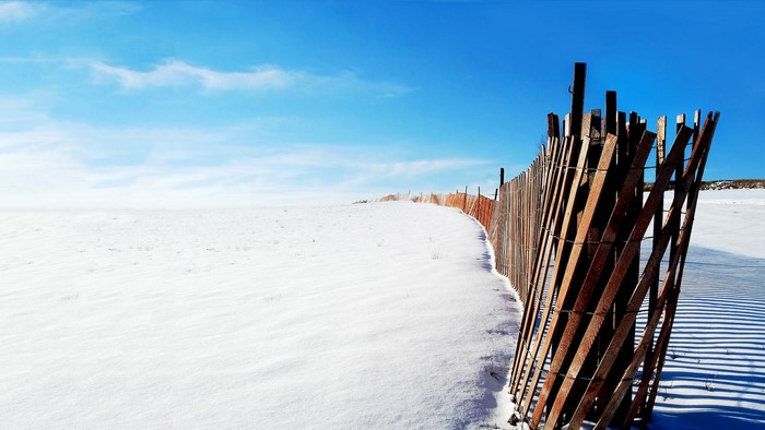 Wooden fence on a snowy beach under a blue sky