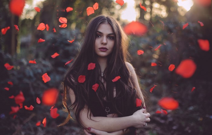 Woman with long dark hair and red petals falling around her