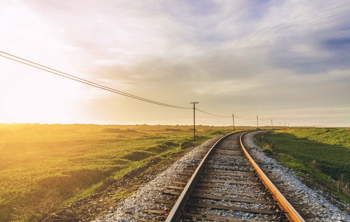 Railway tracks curving through a sunlit field at sunrise