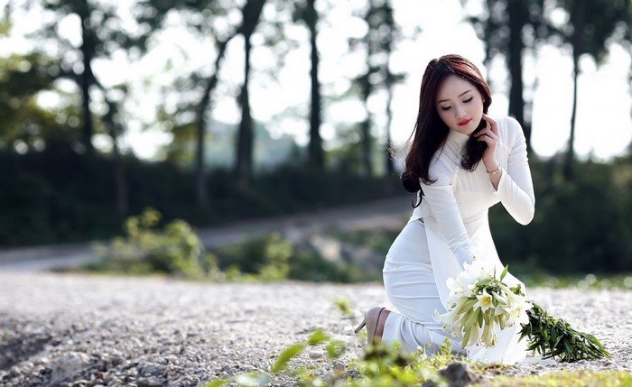 Elegant Woman in White Dress Holding Flowers Outdoors