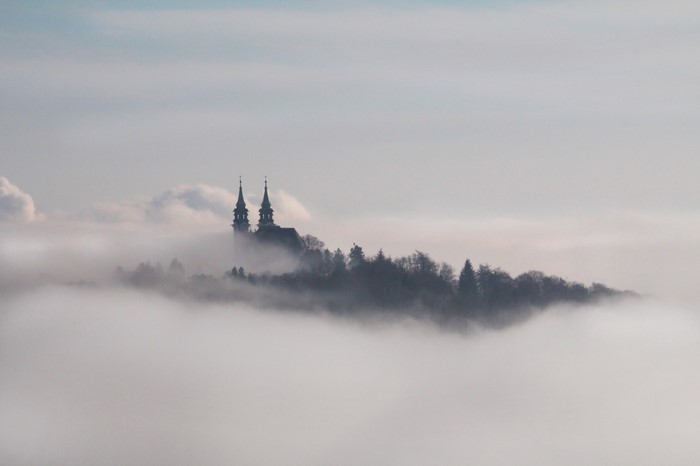 Church towers emerging from fog above a forest