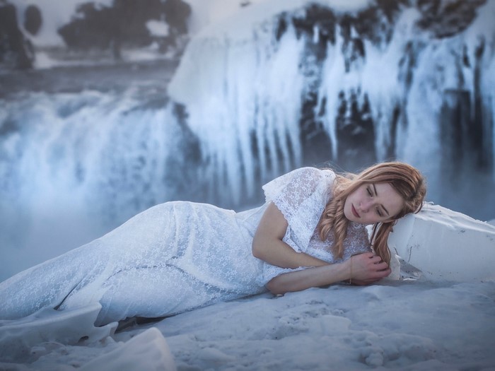 Woman in white dress lying on ice near waterfall