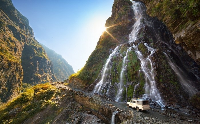 Off-road vehicle driving past a waterfall on a mountain road in Nepal