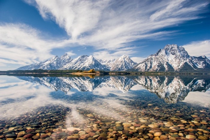 Snowy mountains reflected in a clear lake with pebbles
