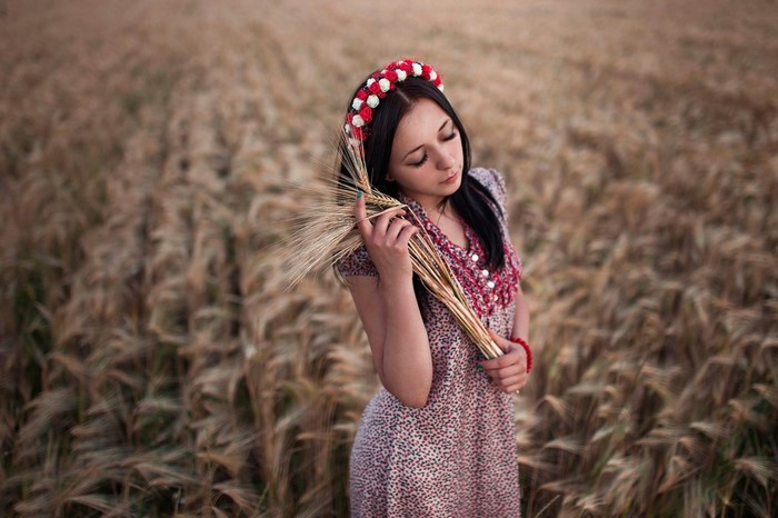 Woman with flower crown in wheat field holding wheat stalks