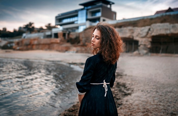 Woman in black dress on beach with modern building