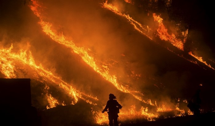 Firefighter silhouetted against a raging wildfire