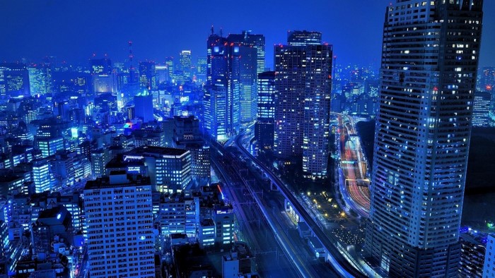 Blue illuminated cityscape at night with skyscrapers and train tracks
