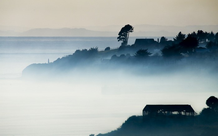 Misty coastal landscape with houses and a lighthouse