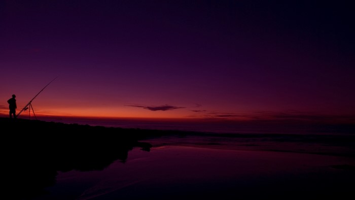 Fisherman with rod at sunset on the coast
