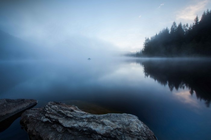 Misty lake with a lone boat and forest reflection