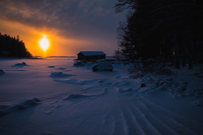 Winter sunset over a frozen lake with a small hut