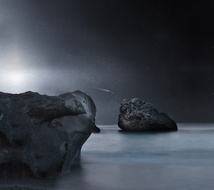Night sky with stars and a shooting star over rocks in the ocean