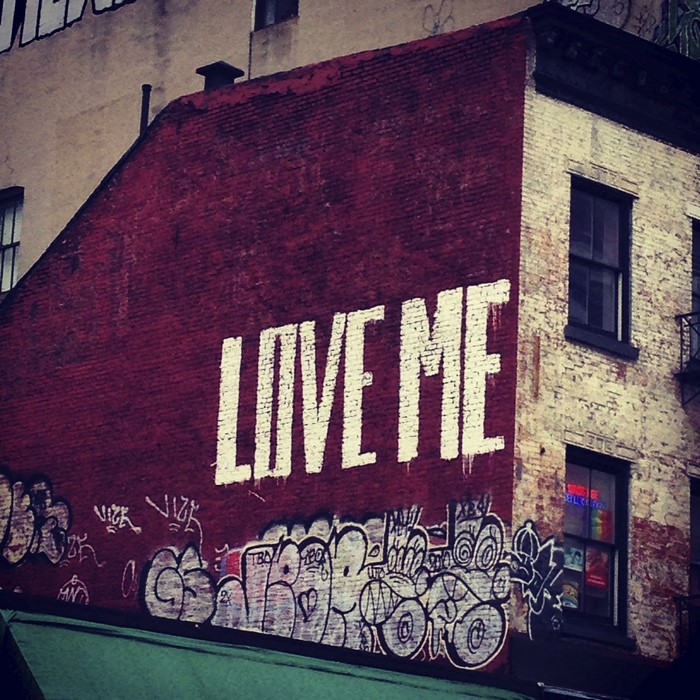 Graffiti on a brick wall with "LOVE ME" text