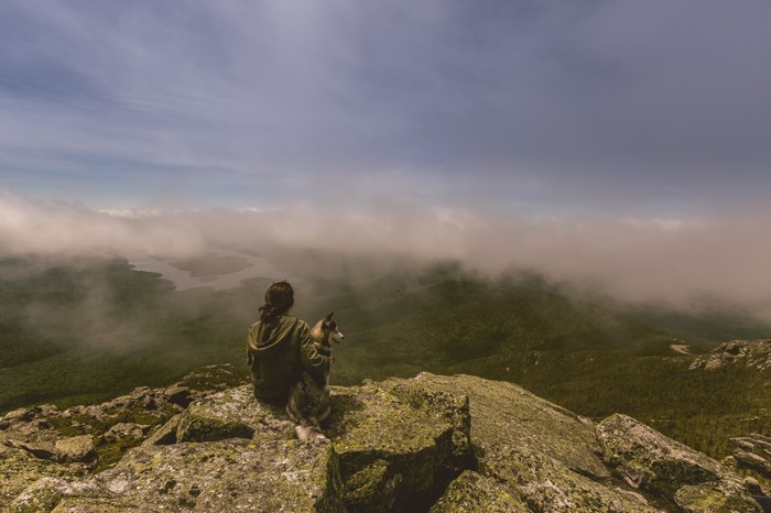 Woman and dog on mountain summit overlooking misty valley