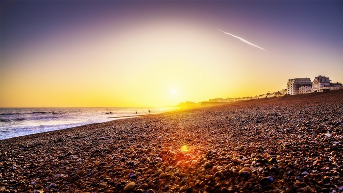 Sunset over a pebble beach with buildings on the coast