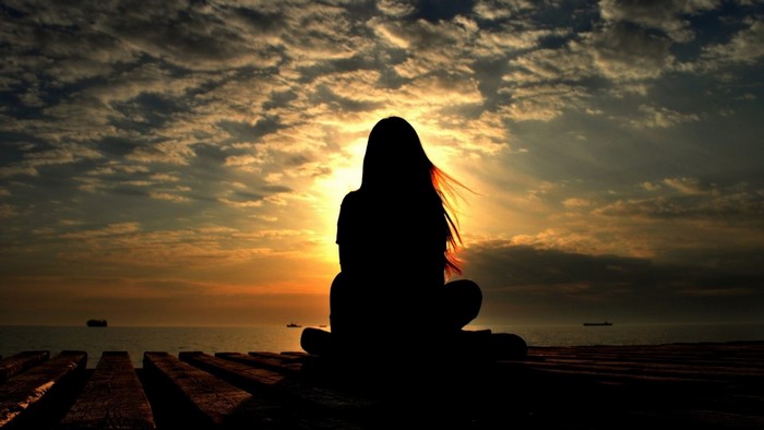 Silhouette of a person meditating by the sea at sunset