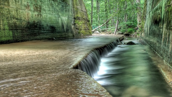 Waterfall flowing through a moss-covered concrete channel in a forest