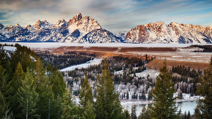 Snow-capped mountains over a winter valley with pine trees