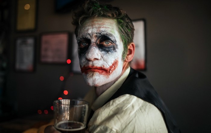 Man dressed as the Joker holding a glass of beer