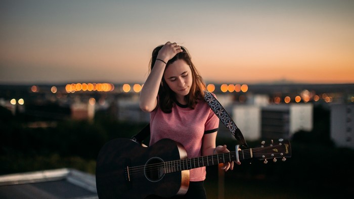 Woman with guitar on rooftops at sunset
