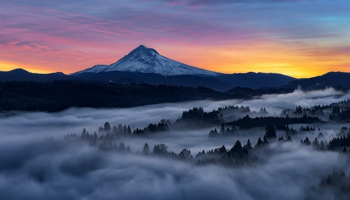 Snowy mountain peak at sunrise over misty forest