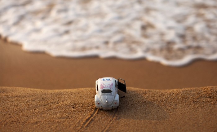 Toy Volkswagen Beetle on a sandy beach with waves