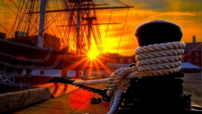 Tall ship docked at harbor during sunset with sun rays