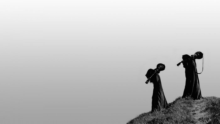 Two figures in robes carrying guitars on a hill