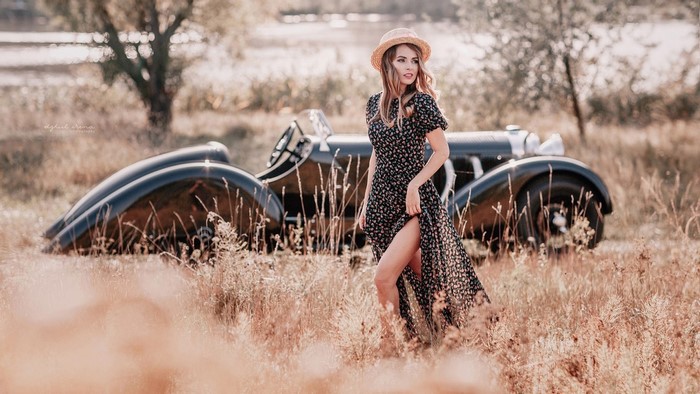 Woman in floral dress and hat with vintage car