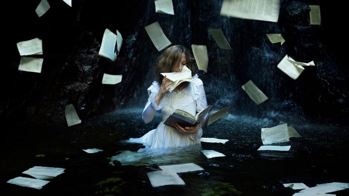 Woman in white dress reading a book in water with falling pages