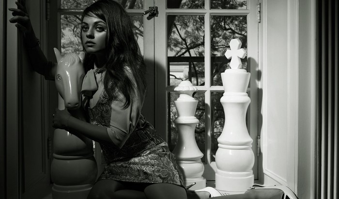 Mila Kunis posing with chess pieces and a horse sculpture