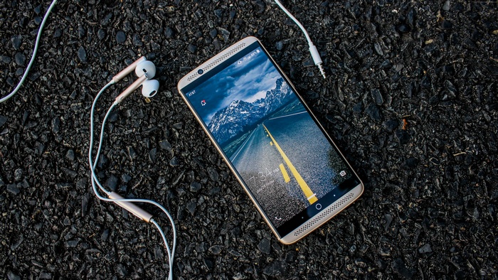 ZTE Gigabit smartphone with earbuds on asphalt