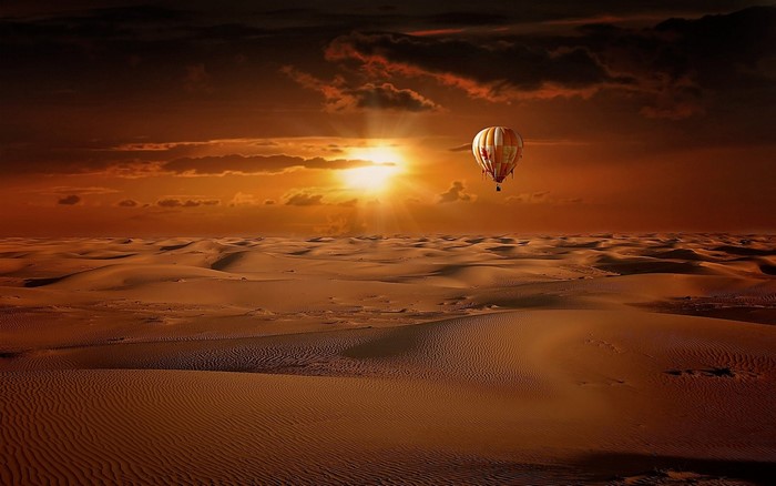 Hot air balloon over desert dunes at sunset