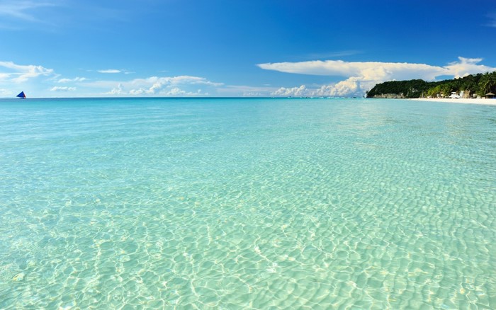 Crystal clear turquoise water on a tropical beach with a sailboat
