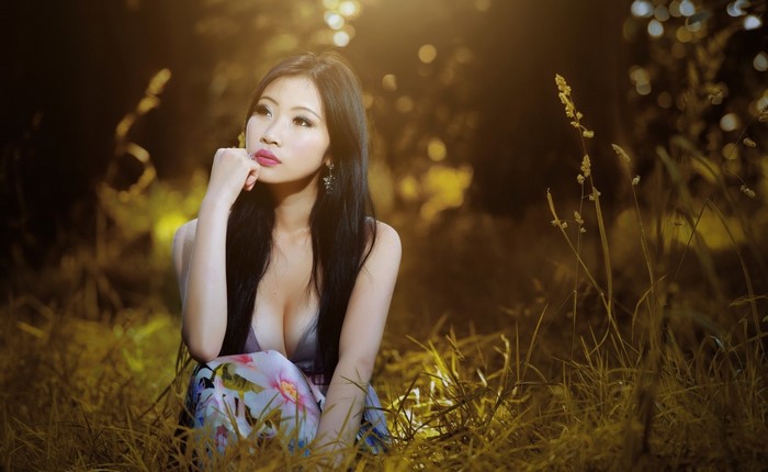 Asian woman sitting in tall grass with sunlight
