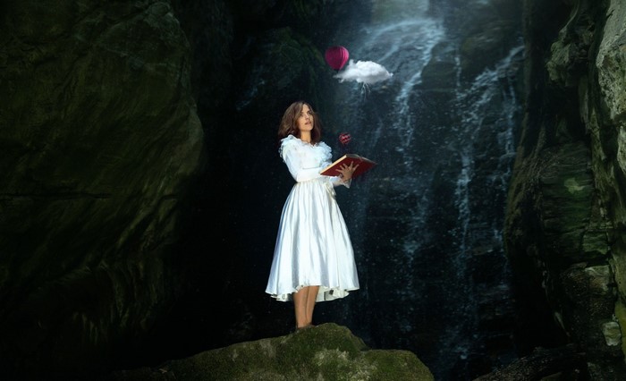 Woman in white dress holding a book near a waterfall