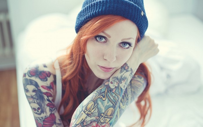 Woman with red hair and tattoos wearing a blue beanie
