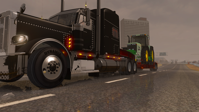 Black semi-truck hauling a tractor on a wet highway