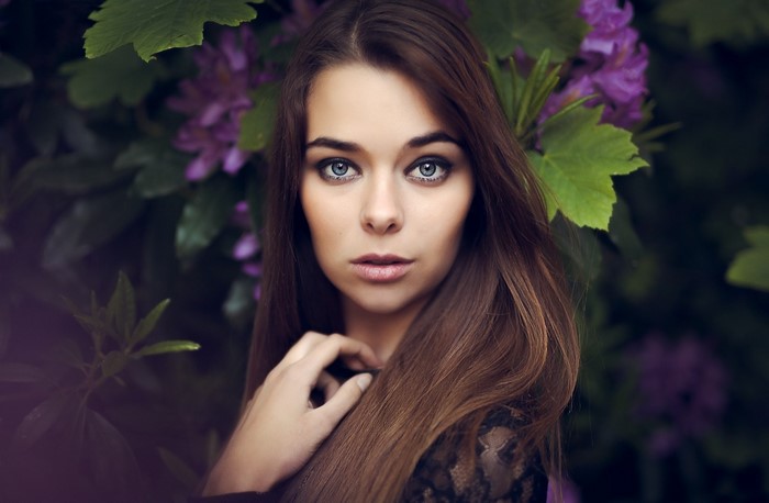 Woman with blue eyes and brown hair in front of purple flowers