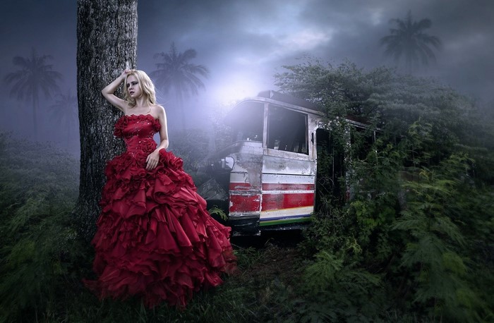 Woman in red dress by a tree near a bus