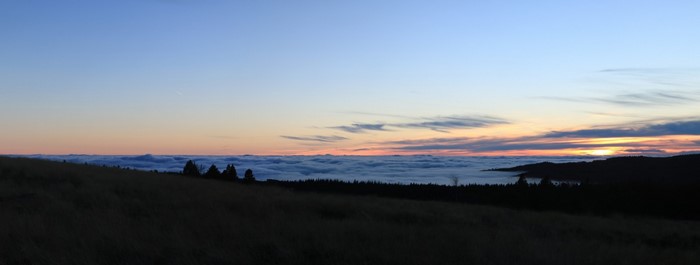 Sunset over a sea of clouds from a grassy hill