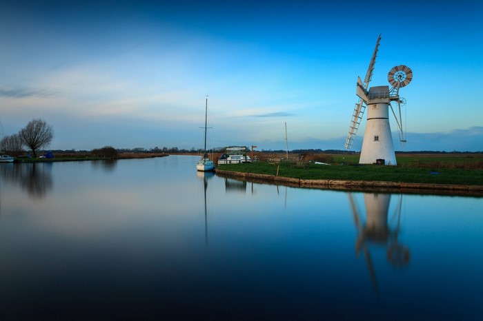 Windmill and boats on a calm river at dusk