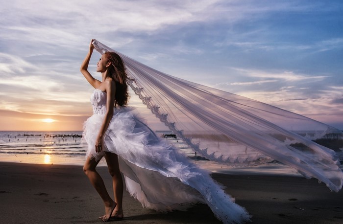 Woman in wedding dress on beach at sunset