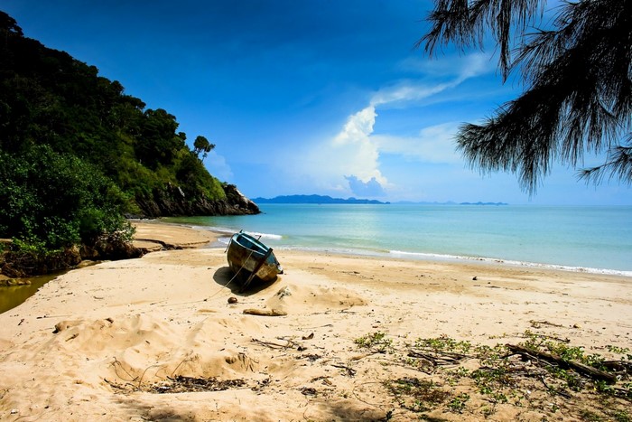 Boat on a sandy beach with a lush green hill and blue ocean